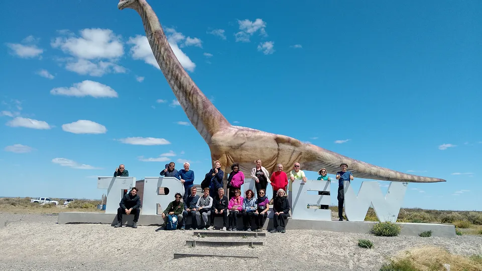 Gruppo di persone che posano davanti alla scritta Trelew con dinosauro